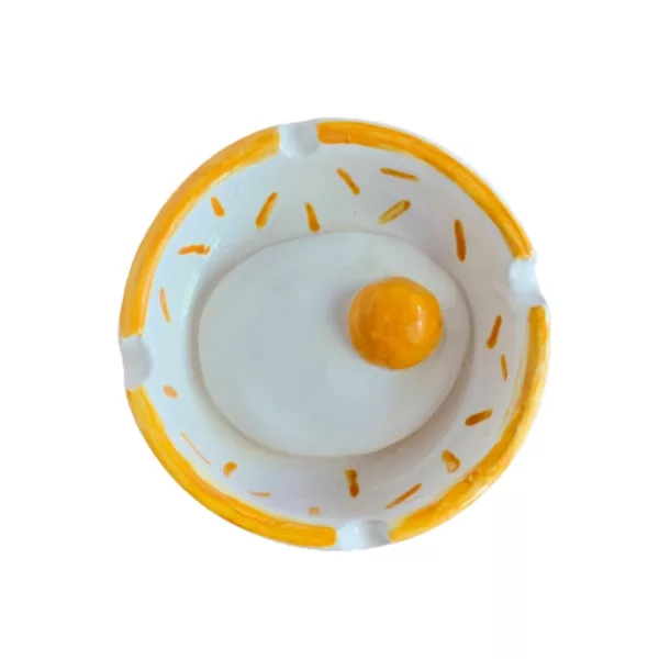 White ceramic ashtray with yellow yolk in center. Small hole for yolk, decorated with white dots. Simple and minimalist design.