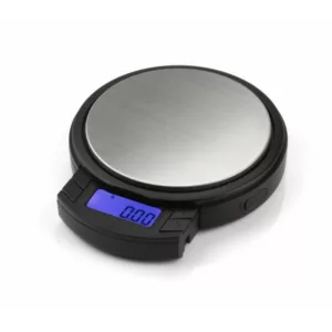 Electronic scale with black and silver casing, blue display, and small round base. Displays weight in grams and kilograms. Has a small black button for turning on and off. White background.