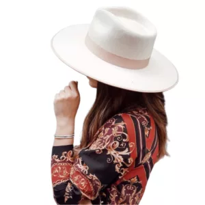 Floral print blouse, black pants, and white hat with red and pink flowers. Woman looking down, possibly checking phone. Blurred outdoor background.