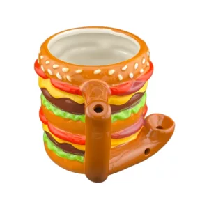 Ceramic mug shaped like a giant burger with 'Roast & Toast' written on it, featuring a toothpick, brown base, pickle handle, and lettuce decoration on the bottom.