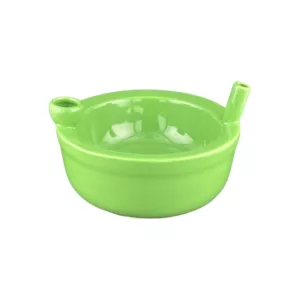 Green ceramic bowl with long handle and small spout, filled with cereal. Handle and spout made of same material as bowl. Transparent surface. White background.