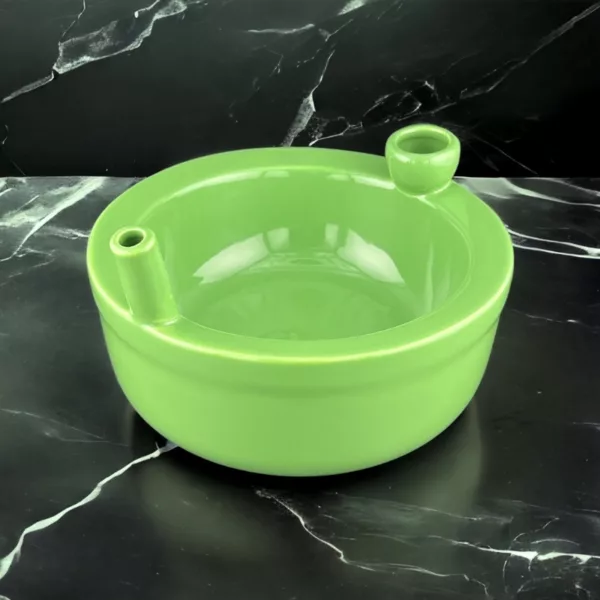 Green ceramic bowl with small hole on black marble countertop, showing condensation.