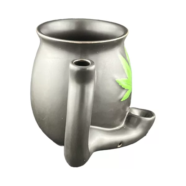The Matte Black Mug With Green Leaf by Roast And Toast features a metal mug with a marijuana leaf design on the side, sitting on a white background.