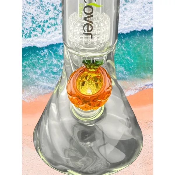 Glass pineapple bowl with orange slice and stem, set against beach waves.