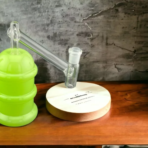 Green glass beaker on wooden table. Clear, cylindrical shape. Wooden surface with rough texture and stains. Rectangular table with smooth surface and same wood type.