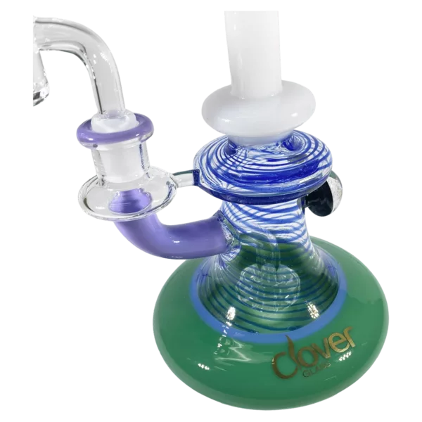 unique bong with a green and blue base and purple stem, made of clear glass with intricate designs. It has a small hole at the top and is listed on a smoking company website.