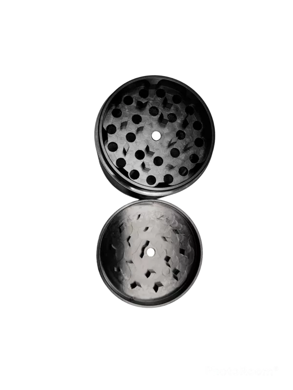 Circular metal grinder with black and white design and small holes on edges, placed on green background.