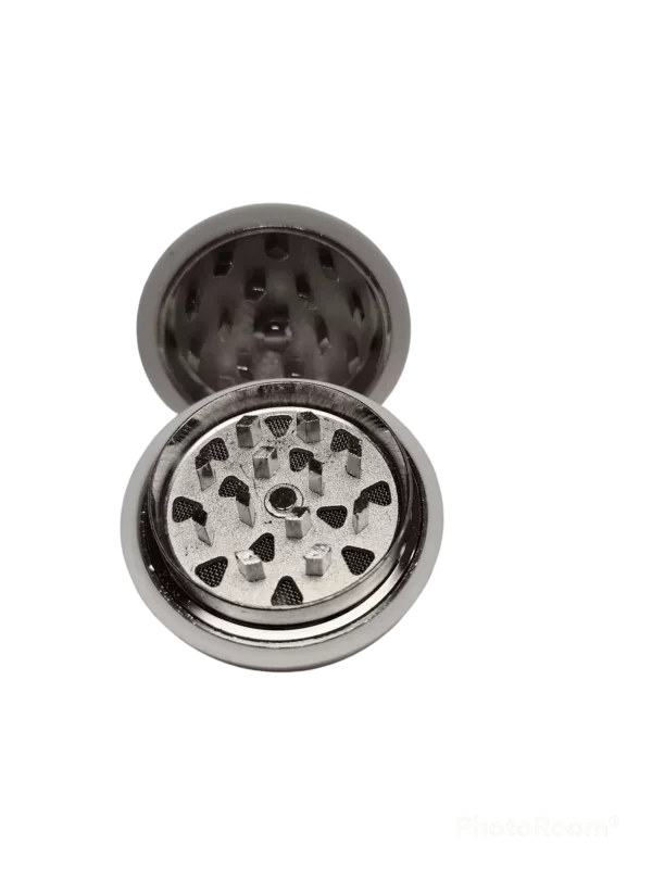 Stainless steel grinder with circular shape and raised edge with small holes for herb grinding. Disc rotates for grinding. In focus, gray and black colors with occasional silver highlights.
