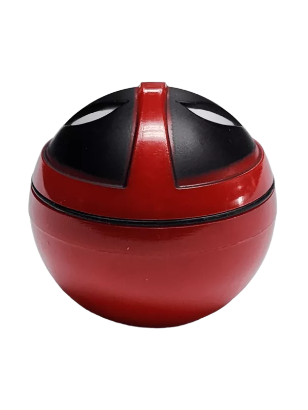 Red and black container with face-shaped hole, sitting on green surface with small bubble emerging.