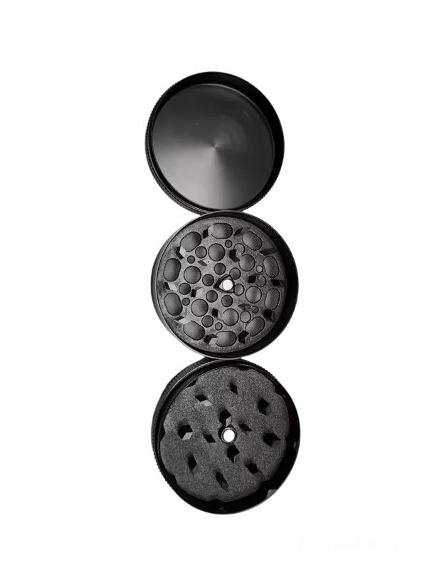 high-quality black metal grinder with a circular shape and open lid, revealing the contents inside. The image is taken from a side view and the background is green.