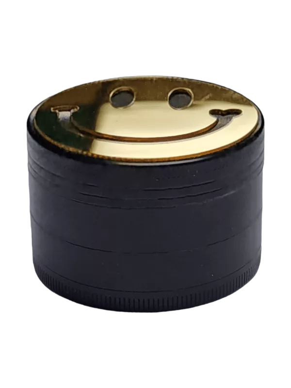 Black and gold metal grinder with a smiling face and circular shape. Flat bottom and smooth sides. No other features.