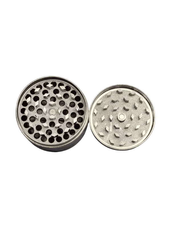 The Qute Cannabis Print Grinder has a circular shape with a small hole in the center, made of metal with a silver finish. It is designed to grind herbs or spices and is shown on a green background.