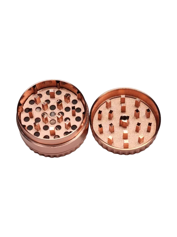 well-made copper or brass grinder with evenly spaced holes and a small button on the front. It is in good condition and stands out against a green background.