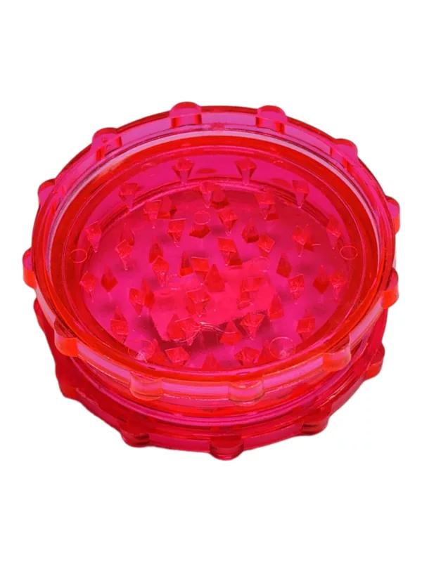 Red plastic grinder with clear lid and small hole in center. Round container with smooth surface, sits on white background.