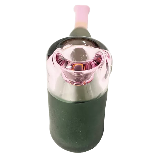 A small glass bottle with a pink cap and green base, featuring a small hole at the top and sitting on a green surface.