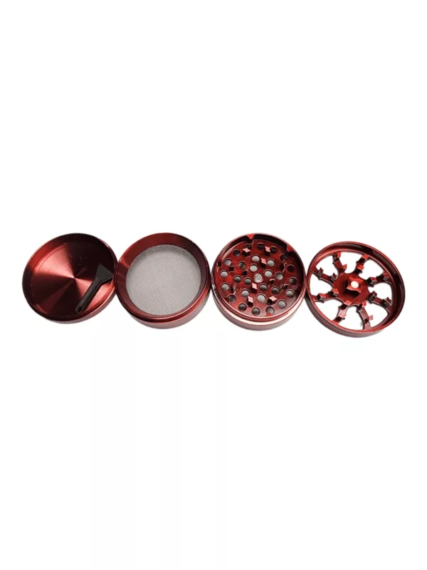 A red metal grinder with a circular shape, handle, and small hole in the center. It has a small circular piece on top and sits on a white background.