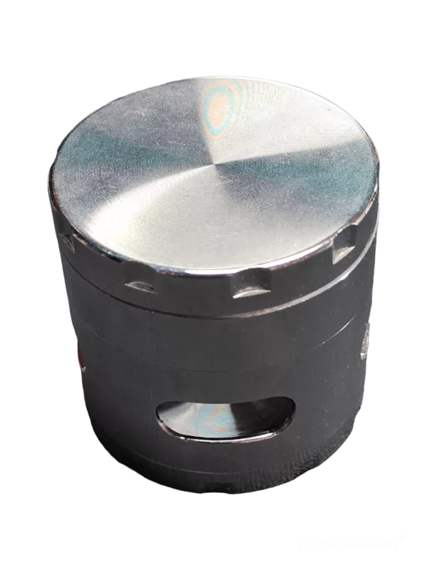 Metal round grinder with black handle and silver rim. Smooth surface, screw attachment, raised rim. Green background.
