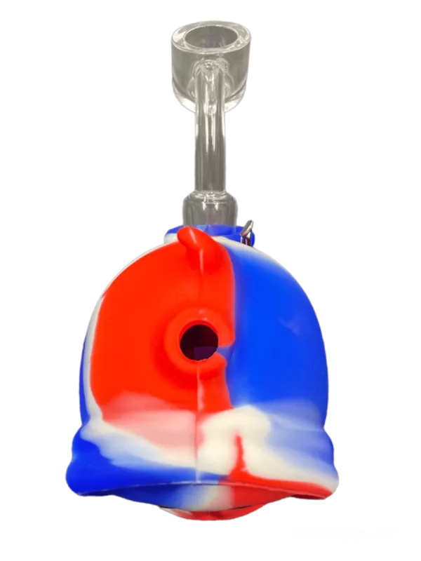 Red, white, and blue glass bong with clear base and blue and red spout. White base with green background. Made of glass.
