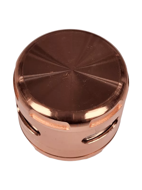 The Zinc Window Grinder by BVGS077 is a small, circular metal container with a flat surface and a copper-colored finish. It is intended for use in grinding and storing dry herbs. The image is not clear enough to determine the size or shape of the container.