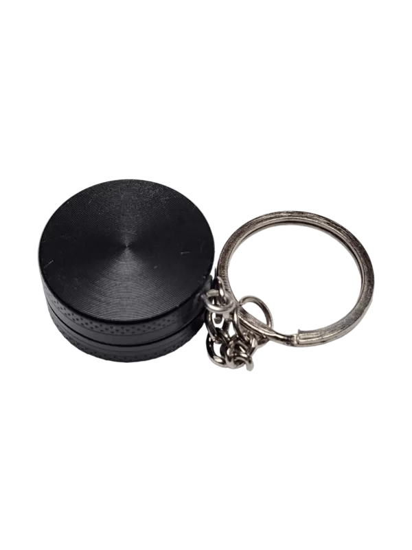 Small circular keychain grinder made of black plastic with a chain and lock. Well-lit image.