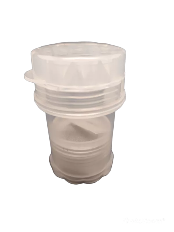 Plastic bottle grinder with 4 parts, designed for grinding herbs and spices into powder. Clear body and sits on white countertop.