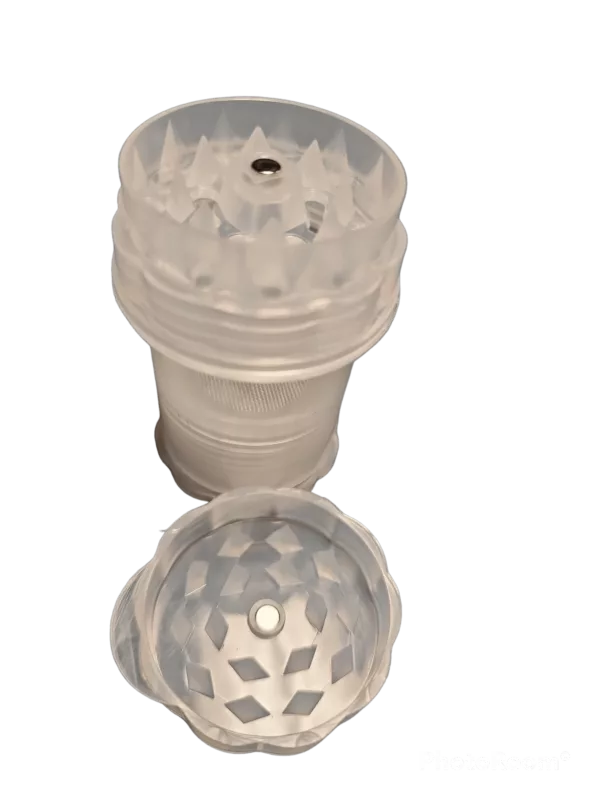 A transparent plastic container with a lid and a small hole on top, sitting on a green surface. It is a 4-part plastic bottle grinder.