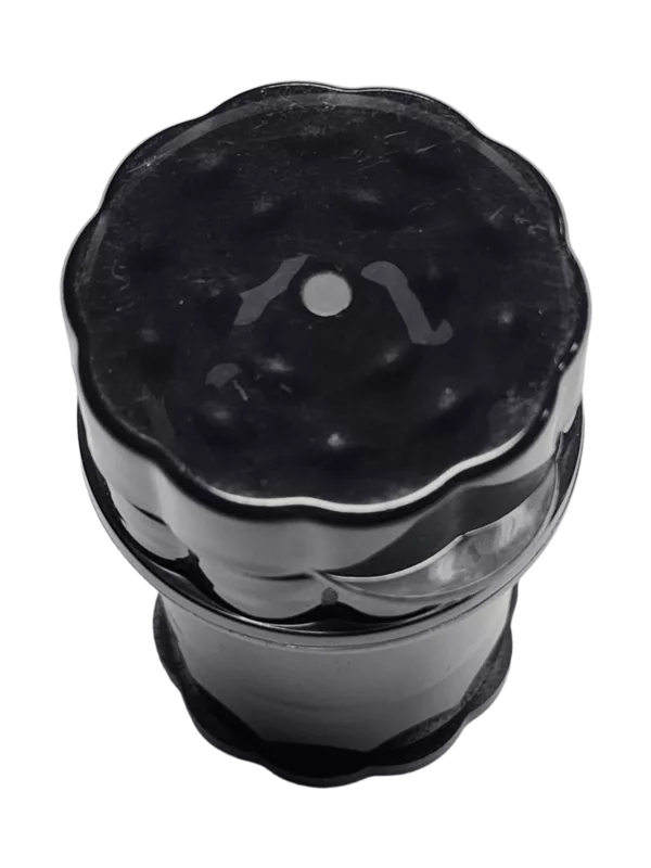 Black plastic round container with a small hole on top for convenient use. Smooth surface and green background. Ideal for storing and grinding smoking supplies.